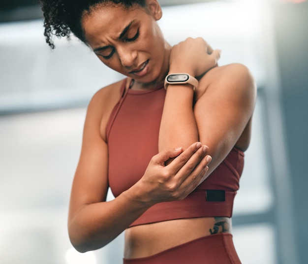 Dolore al gomito e fitness con una donna di colore sportiva in palestra con un'articolazione dolorante da un allenamento fisico Allenamento e salute con una giovane atleta alle prese con un braccio o un muscolo ferito