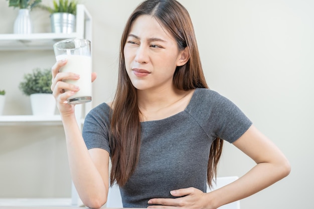 Dolore allergia asiatica giovane donna ragazza mano nella pancia soffrire dopo aver bevuto un bicchiere di latte infelice e cattivo mal di stomaco Intolleranza al lattosio e latticini concetto di problema di salute