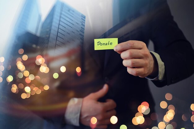 Donazione di beneficenza nel concetto di business L'uomo d'affari mostra una carta con la parola dona Grattacielo a doppia esposizione