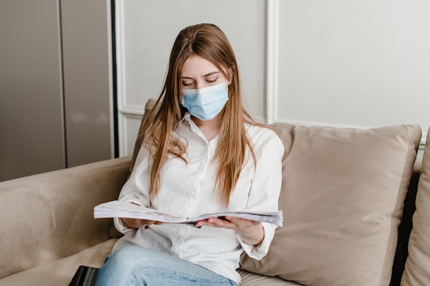 Donna a casa sui libri e sull'apprendimento d'uso della maschera da portare dello strato