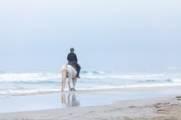 Donna a cavallo sulla spiaggia in una giornata nuvolosa