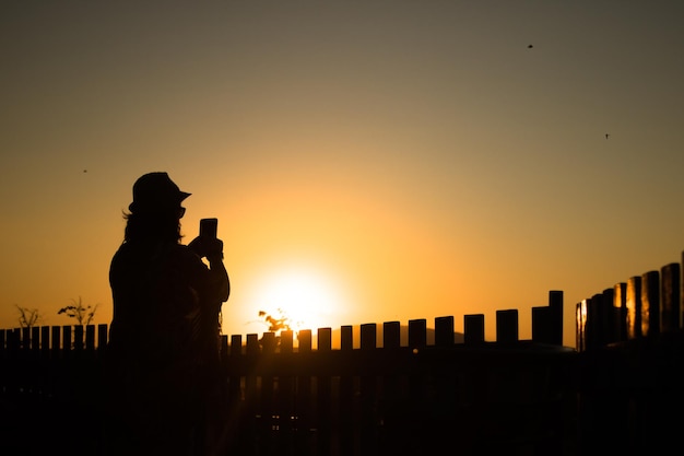 Donna a silhouette che fotografa contro il cielo arancione