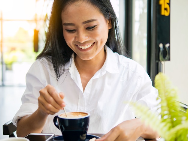 Donna abbastanza asiatica che beve caffè caldo, ritenente disteso, felice