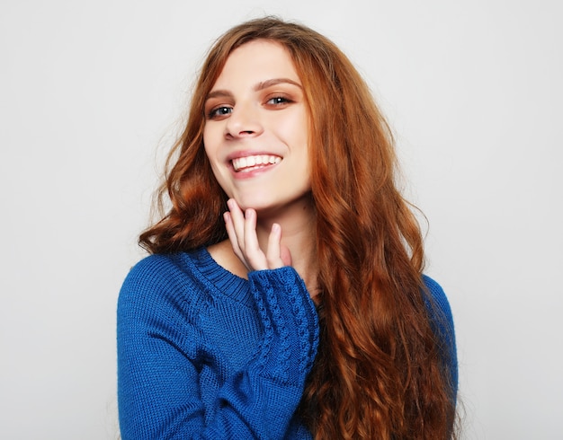 Donna abbastanza bella con capelli ricci che guarda l'obbiettivo che ha emozionato e felice espressione facciale, contro il muro bianco dello studio.