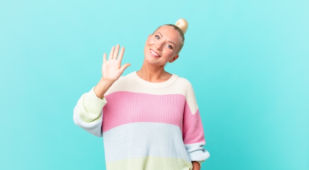 Donna abbastanza bionda che sorride felicemente, agitando la mano, dandoti il benvenuto e salutandoti