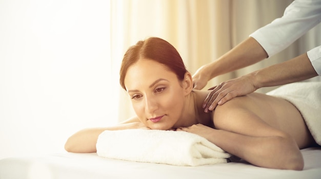 Donna abbastanza castana che gode della procedura di massaggio alla schiena nel salone della stazione termale. Concetto di bellezza.