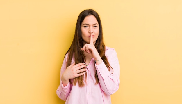 Donna abbastanza caucasica che sembra seria e incrociata con il dito premuto sulle labbra chiedendo silenzio o mantenendo un segreto tranquillo