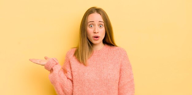 Donna abbastanza caucasica che sembra sorpresa e scioccata con la mascella caduta tenendo un oggetto con una mano aperta sul lato