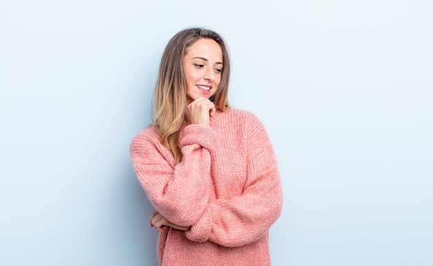 Donna abbastanza caucasica che sorride con un'espressione felice e sicura con la mano sul mento chiedendosi e guardando di lato