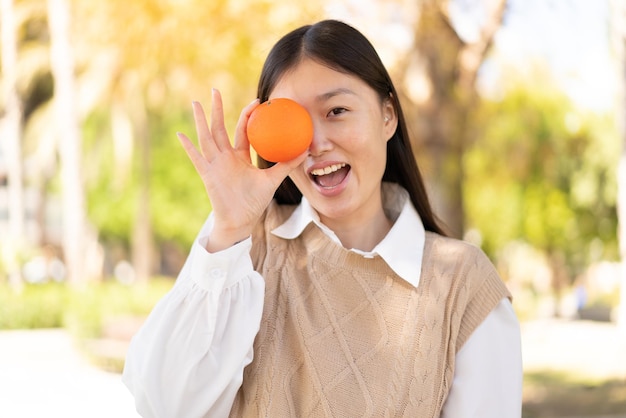 Donna abbastanza cinese all'aperto che tiene un'arancia con l'espressione sorpresa