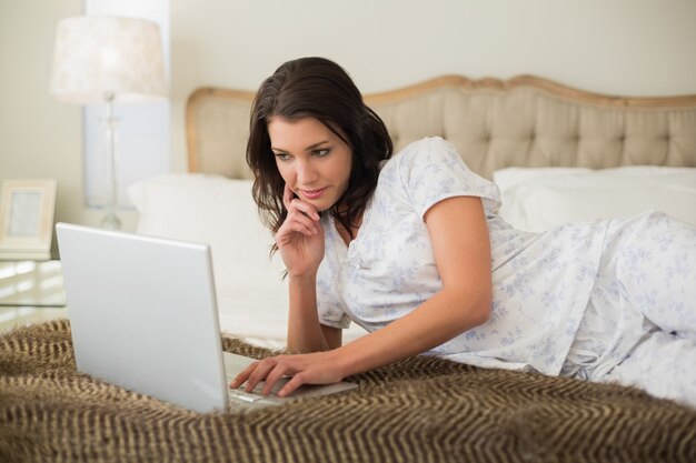 Donna abbastanza dai capelli marrone di pensiero che per mezzo di un computer portatile