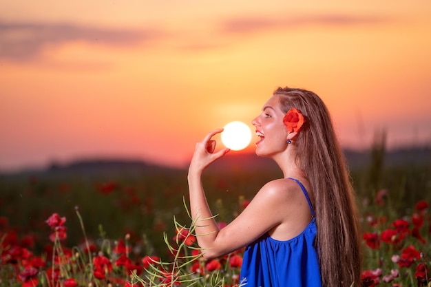 Donna abbastanza giovane che gioca con la palla di sole mentre si trova in un campo di papaveri nella calda luce del tramonto