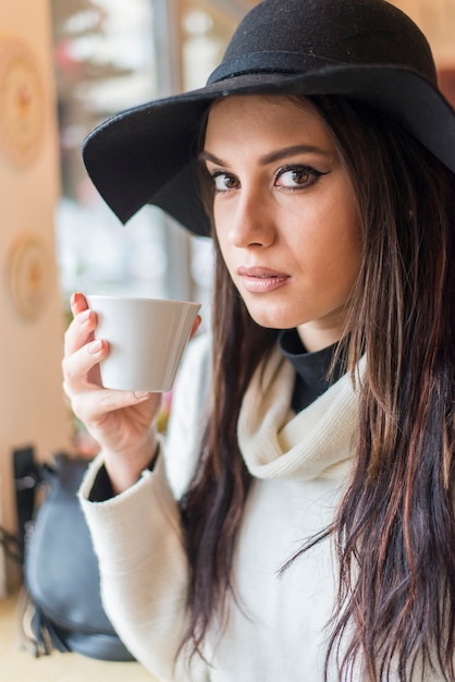 Donna abbastanza giovane con il cappello che beve caffè