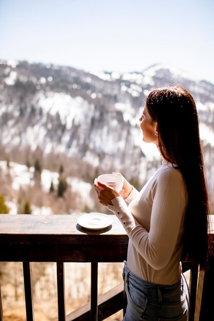 Donna abbastanza giovane con una tazza di tè caldo nella finestra d'inverno