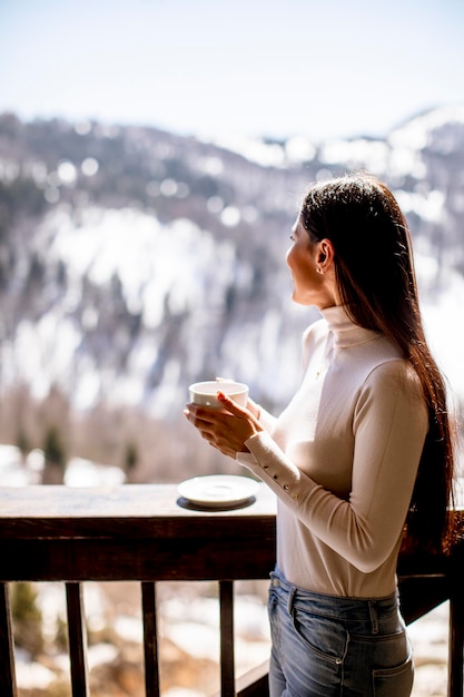 Donna abbastanza giovane con una tazza di tè caldo nella finestra di inverno