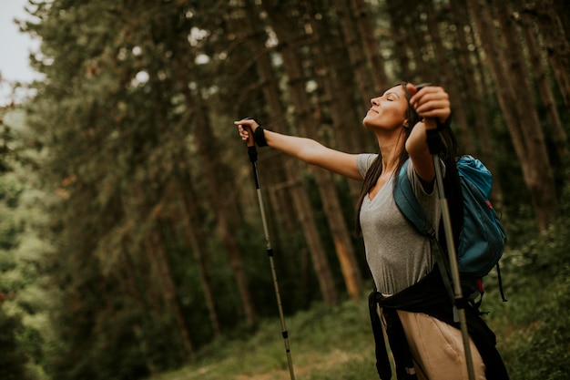 Donna abbastanza giovane del viaggiatore con zaino e sacco a pelo che gode della bella foresta verde intorno a lei