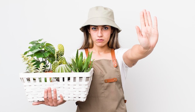 Donna abbastanza ispanica che sembra seria mostrando il palmo aperto facendo il gesto di arresto delle piante e il concetto di giardinaggio