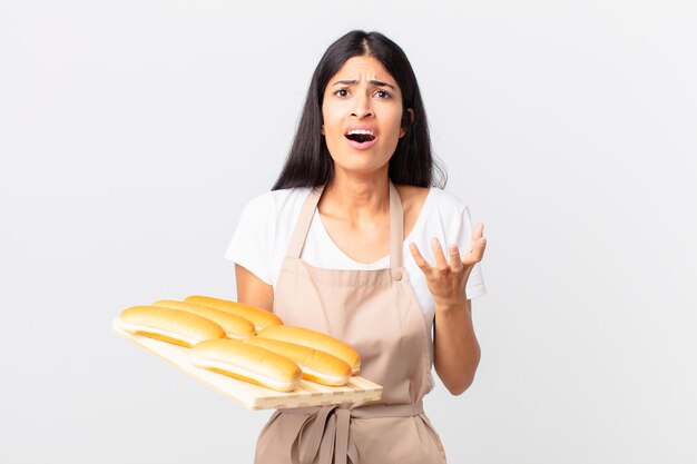 Donna abbastanza ispanica del cuoco unico che sembra disperata frustrata e stressata e tiene in mano un vassoio con focacce di pane