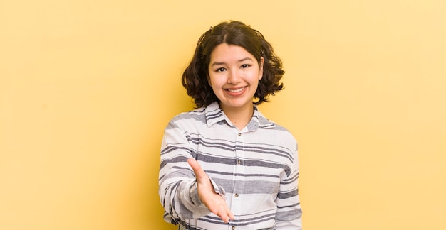 Donna abbastanza ispanica sorridente che sembra felice, sicura di sé e amichevole, offrendo una stretta di mano per chiudere un accordo cooperando