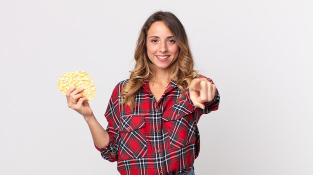 Donna abbastanza magra che indica la macchina fotografica che ti sceglie e che tiene una torta di riso dietetica