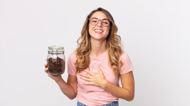 Donna abbastanza magra che ride ad alta voce per qualche scherzo esilarante e tiene in mano una bottiglia di chicchi di caffè