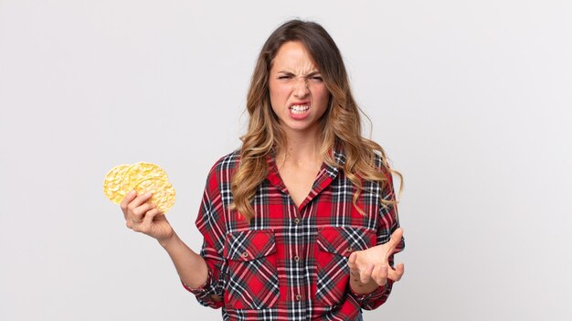 Donna abbastanza magra che sembra arrabbiata, infastidita e frustrata e con in mano una torta di riso dietetica