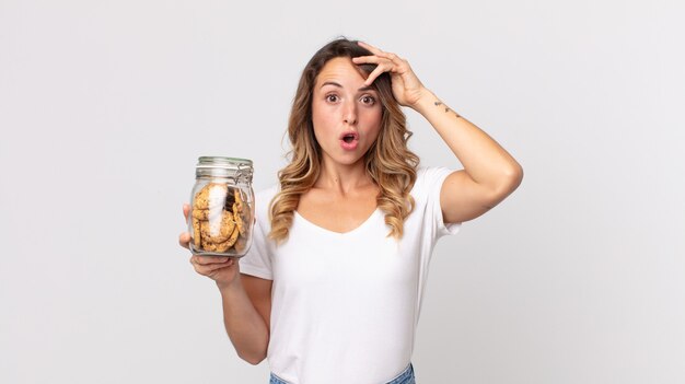 Donna abbastanza magra che sembra felice, stupita e sorpresa e tiene in mano una bottiglia di vetro di biscotti