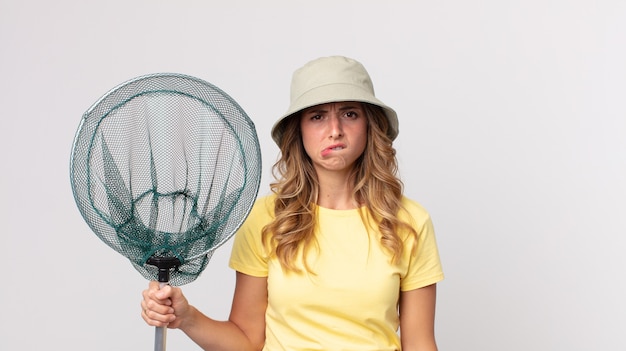 Donna abbastanza magra che sembra perplessa e confusa che indossa un cappello e tiene in mano una rete da pesca