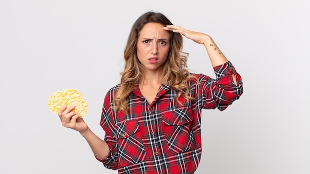 Donna abbastanza magra che si sente confusa e perplessa mostrando che sei pazzo e con in mano una torta di riso dietetica