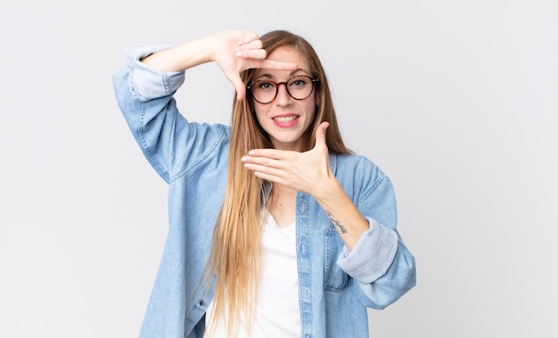 Donna abbastanza magra che si sente felice, amichevole e positiva, sorride e fa un ritratto o una cornice per foto con le mani