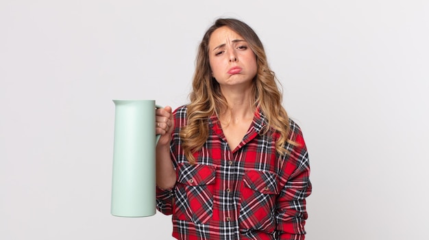 Donna abbastanza magra che si sente triste e piagnucolona con uno sguardo infelice e piange e tiene in mano un thermos di caffè