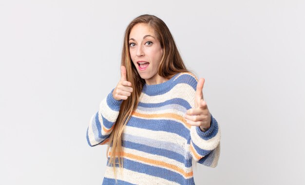 Donna abbastanza magra che sorride con un atteggiamento positivo, di successo e felice che indica la telecamera, facendo il segno della pistola con le mani