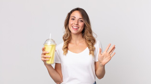 Donna abbastanza magra che sorride felicemente agitando la mano dandoti il benvenuto e salutandoti e tenendo un milkshake alla vaniglia