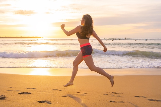 Donna adatta che corre lungo una spiaggia sabbiosa durante il tramonto