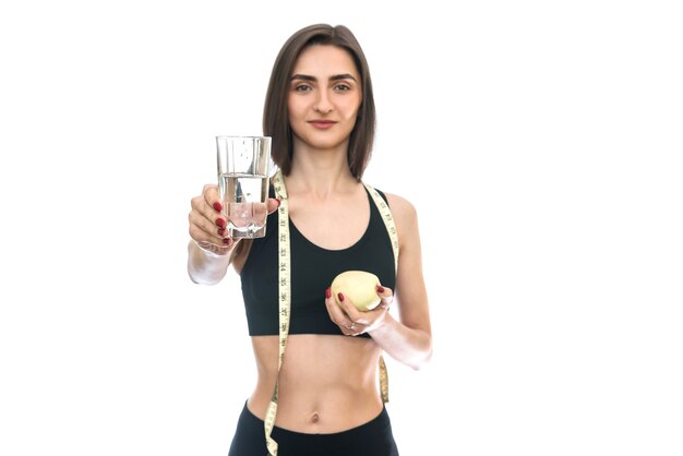 Donna adatta che tiene mela e bicchiere d'acqua isolato su bianco