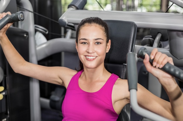 Donna adatta che utilizza la macchina del peso in palestra