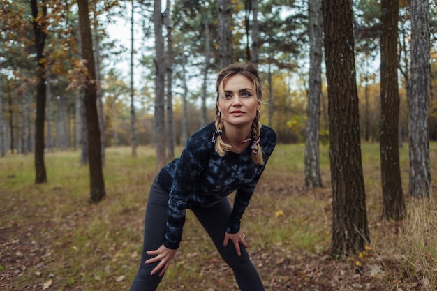 Donna adatta di sport stanco con le trecce che riposa dopo il jogging nella foresta di autunno
