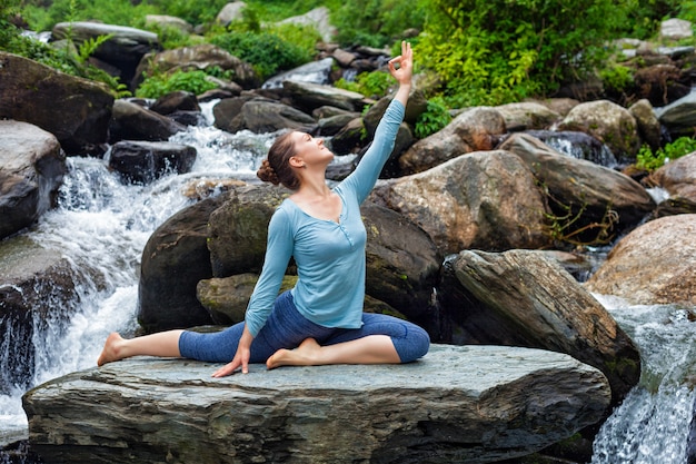 Donna adatta ordinata che fa asana di yoga all'aperto alla cascata tropicale