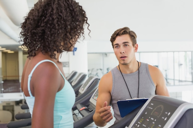 Donna adatta sul tapis roulant che parla con personal trainer