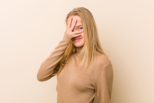 Donna adolescente carina e naturale lampeggia alla macchina fotografica attraverso le dita, imbarazzato volto coprente.