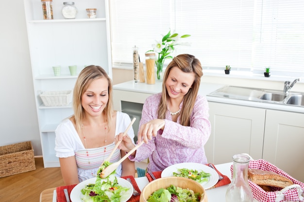 Donna adorabile che serve insalata alla sua amica che si siede a un tavolo durante l&#39;ora di pranzo