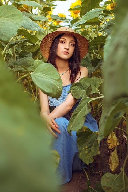 Donna adorabile che si siede fra il giacimento di girasole di fioritura del mazzo giallo all'aperto natura calda di alba