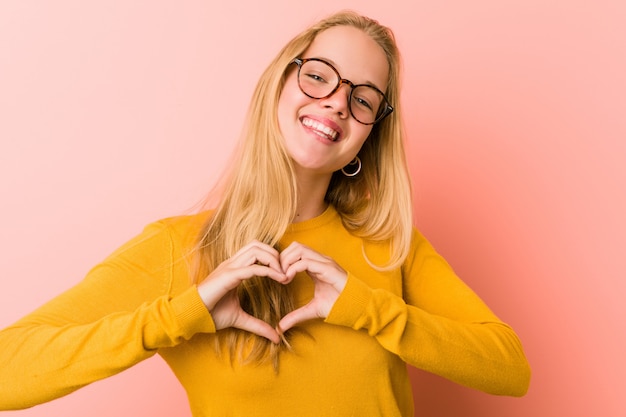 Donna adorabile dell'adolescente che sorride e che mostra una forma del cuore con le mani