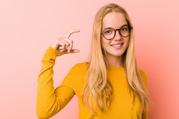 Donna adorabile dell'adolescente che tiene qualcosa di piccolo con gli indici, sorridente e sicuro.