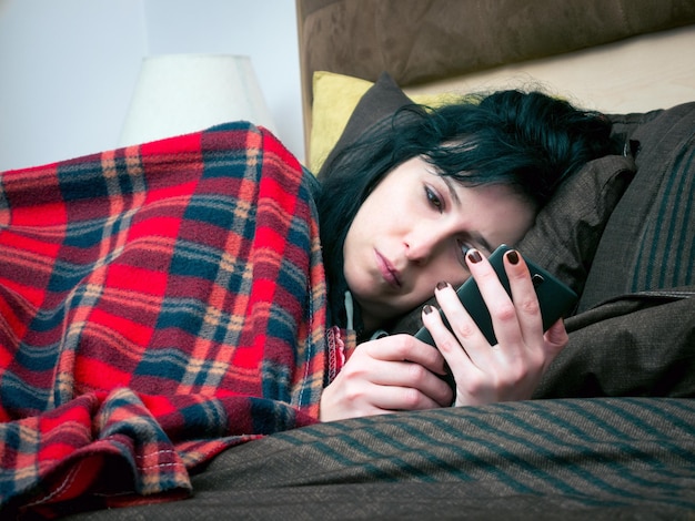 Donna adulta a metà che usa il cellulare mentre è sdraiata a letto a casa