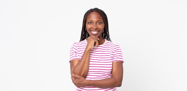 Donna adulta afro nera che sembra felice e sorridente con la mano sul mento, chiedendosi o facendo una domanda, confrontando le opzioni
