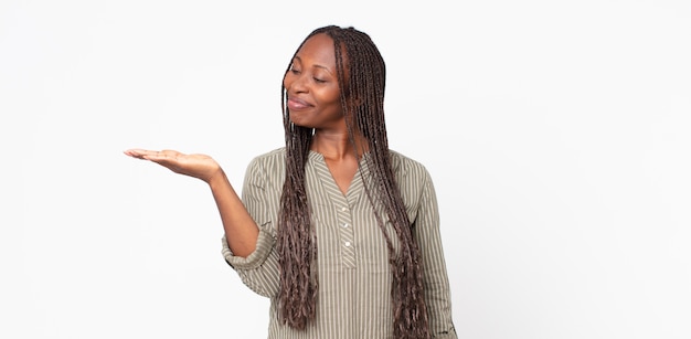 Donna adulta afro nera che si sente felice e sorride casualmente, guardando un oggetto o un concetto tenuto per mano sul lato