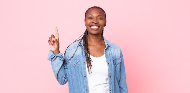 Donna adulta afro nera che sorride allegramente e felicemente, puntando verso l'alto con una mano per copiare lo spazio