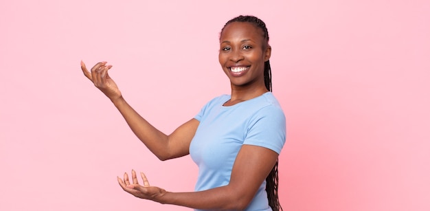 Donna adulta afro nera che sorride con orgoglio e fiducia, sentendosi felice e soddisfatta e mostrando un concetto sullo spazio della copia