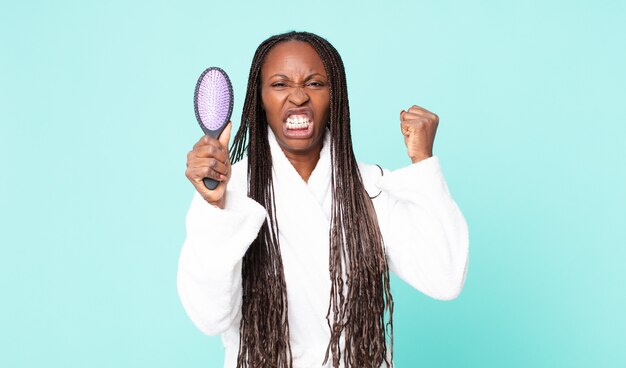 donna adulta afroamericana nera che indossa un accappatoio e tiene in mano una spazzola per capelli